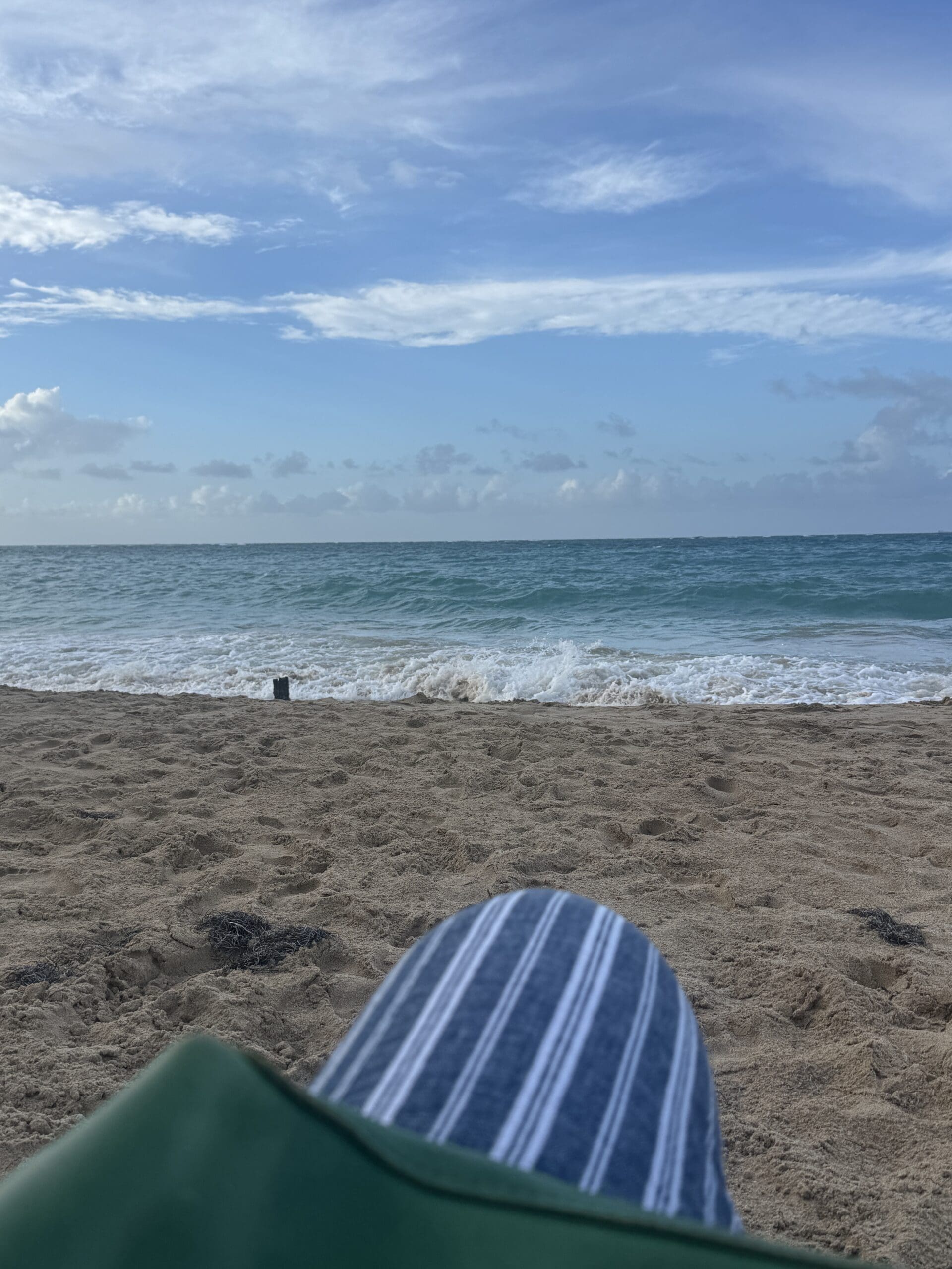 A peaceful day on the beach with a view of the water and sky, captured from a seated perspective of someone sitting and relaxing.